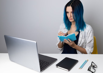 Serious hipster woman with blue hair checking information at laptop online