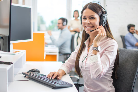 Friendly female helpline operator with headphones in call center