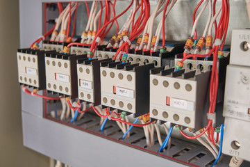 A series of magnetic starters or contactors with additional contacts and electrical wires connected to them in an electrical Cabinet. The wires are connected according to the project.