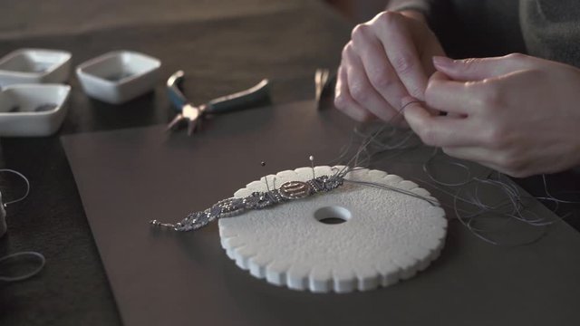 Lifestyle concept, reinvent your life and your job: close-up detail in low angle view of woman hands making macrame knotted bracelet with the fingers knotting the nylon thread on the kumihimo