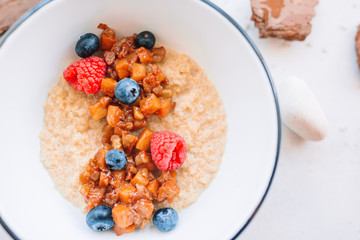 Oatmeal porridge in bowl topped with fresh blueberries, cranberries and homemade crunchy granola