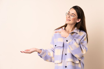 Young woman over isolated beige background holding copyspace imaginary on the palm to insert an ad
