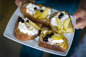 Woman holds white plate with Homemade rispbread toast with Cottage Cheese, sliced apples and black curant