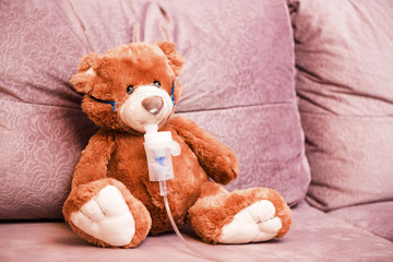 Child makes the procedure to his toy, Teddy Bear with an inhaler nebulizer. Inhalation at home for cough health allergy