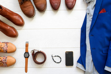 Flat lay set of brown shoes circled around mens blue suit with shirt on white wooden background.