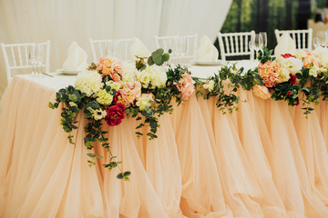 Close up of wedding presidium in restaurant. Wedding banquet table for newlyweds with colorful flowers and beige satin.