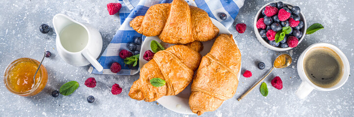 Sweet breakfast butter croissants with coffee cup, orange jam and fresh summer berries. Traditional continental breakfast with croissants concept, grey stone background copy space