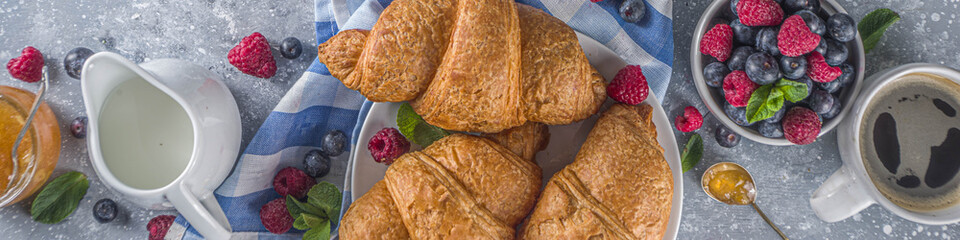 Sweet breakfast butter croissants with coffee cup, orange jam and fresh summer berries. Traditional continental breakfast with croissants concept, grey stone background copy space