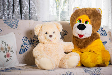 Two toys, friends a big plush bear and a big plush lion on a soft sofa at home
