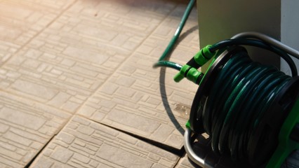 Bright green watering garden hose near old stone floor house with sunlight.