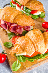 Homemade croissant sandwiches with ham, cheese, fresh vegetables and herbs,