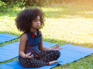 Cute African girl with afro hair doing meditation on yoga mat in the garden.