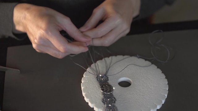 Lifestyle concept, reinvent your life and your job: close-up detail in low angle view of woman hands making macrame knotted bracelet with the fingers knotting the nylon thread on the kumihimo