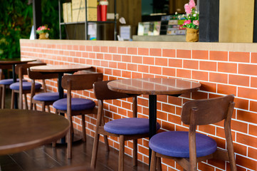 Round wooden tables and chairs on blurred brick wall background in cafe