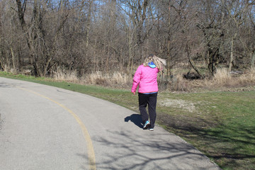 Woman with blonde hair blowing in the wind in a pink coat walking on the North Branch Trail at Chicago's Bunker Hill Woods