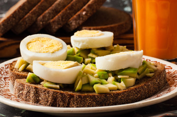 A glass of juice, sandwiches with avocado and egg, black whole grain bread. The concept of diet and proper nutrition