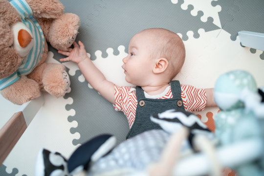 Cute Baby Boy On A Pastel Playmat, Playing With Hanging Rattle Toys. Kids Activity And Play Center For Early Infant Development. Child Kicking And Grabbing Toy. Concept Of Development Of The Newborn.