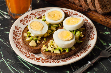 A glass of juice, sandwiches with avocado and egg, black whole grain bread. The concept of diet and proper nutrition