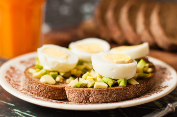 A glass of juice, sandwiches with avocado and egg, black whole grain bread. The concept of diet and proper nutrition