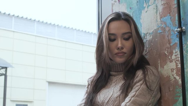 closeup on stylish asian thoughtful pretty girl wearing beige sweater with long hair sits, thinks at cozy cafe. young beautiful female sitting at restaurant alone, looking at window bored. Close up