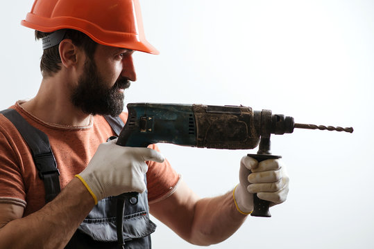 Bearded young builder in helmet. Man using drill. Repairer man in protective hard hat.