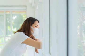 close up young asian woman wear face mask in the living room with looking outside window for quarantine and social distance concept