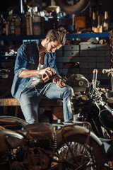 A young man with a hipster look works in his workshop repairing vintage motorcycles.