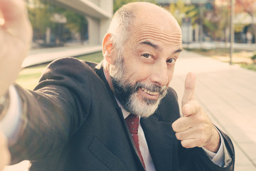Happy businessman smiling at camera. Close-up view of happy handsome mature businessman pointing at camera outdoors. Communication concept