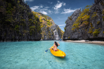 Woman paddling a kayak in the island lagoon between mountains. Kayaking in El Nido, Palawan, Philippines.