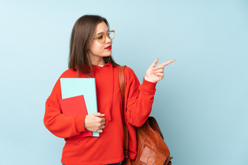 Student girl holding books isolated on blue background pointing finger to the side