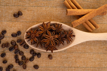 Wooden spoon with star anise on the table on a napkin, next to coffee beans and cinnamon sticks close-up.
