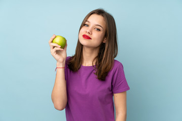 Teenager girl isolated on blue background with an apple and happy