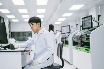 young male scientist looking results from automation blood analyzer report in computer and young female scientist working with automation blood analyzer at medical laboratory