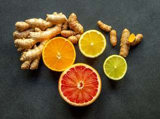 Various types of citrus fruit cut into slices, turmeric, and ginger on the black backboard. Close up