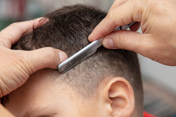 The hairdresser cuts the boy's hair with a razor