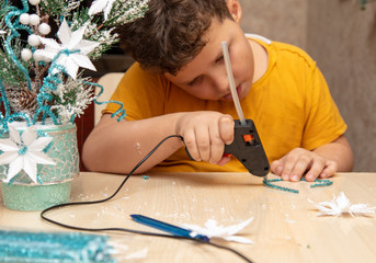 A boy glues snowflakes on a Christmas tree