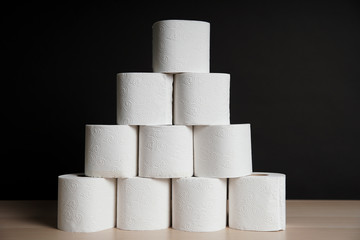 Many toilet paper rolls stacked in pyramid shape. Soft hygienic paper. Wooden table on black background
