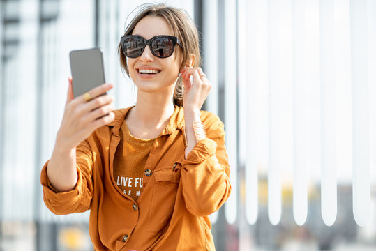 Young woman having a video call on mobile phone while sitting at the transport stop outdoors. Online communication concoept
