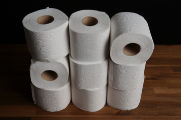 Many toilet paper rolls piled in a heap. Soft hygienic paper. Wooden table on black background.