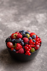 Black bowl with fresh summer berries on a gray background.