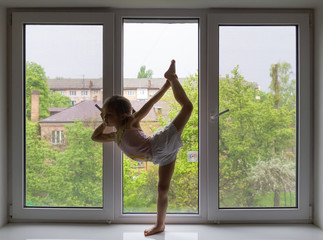 Small girl training on windowsill at home on spring day