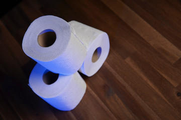 Many toilet paper rolls stacked in a pile, illuminated by a blue lamp. Soft hygienic paper. Wooden table on black background.