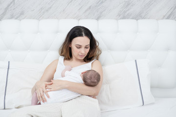 Young mother breastfeeds a newborn baby in her bedroom on the bed