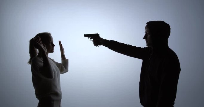 Silhouette of a woman surrenders to the criminal with a gun