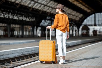 Young female traveler standing with a suitcase at the old train station alone. Travel concept