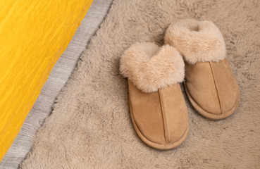 Furry soft slippers on the carpet near the bed. Cozy. Stay at home.