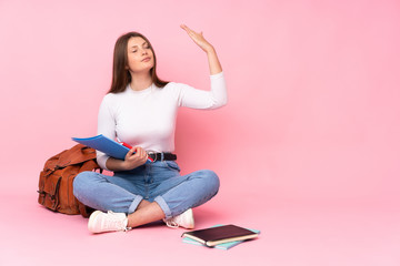 Teenager caucasian student girl sitting on the floor isolated on pink background with tired and sick expression