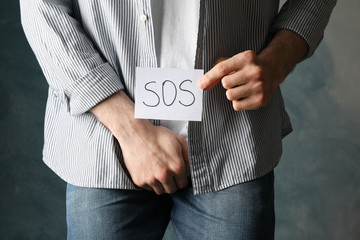 Man holds his crotch and inscription Sos on blue background, close up