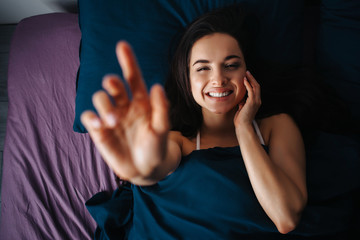 Young beautiful woman in morning bed at home. Positive cheerful woman smile. Touch her face and...