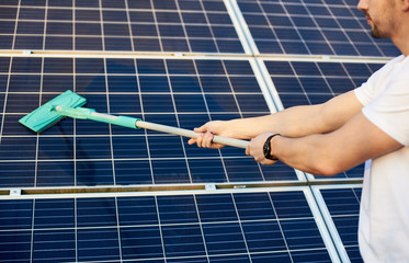 Man hands with a clock cleaning solar panels after installation outdoors. Close up. Solar energy concept image